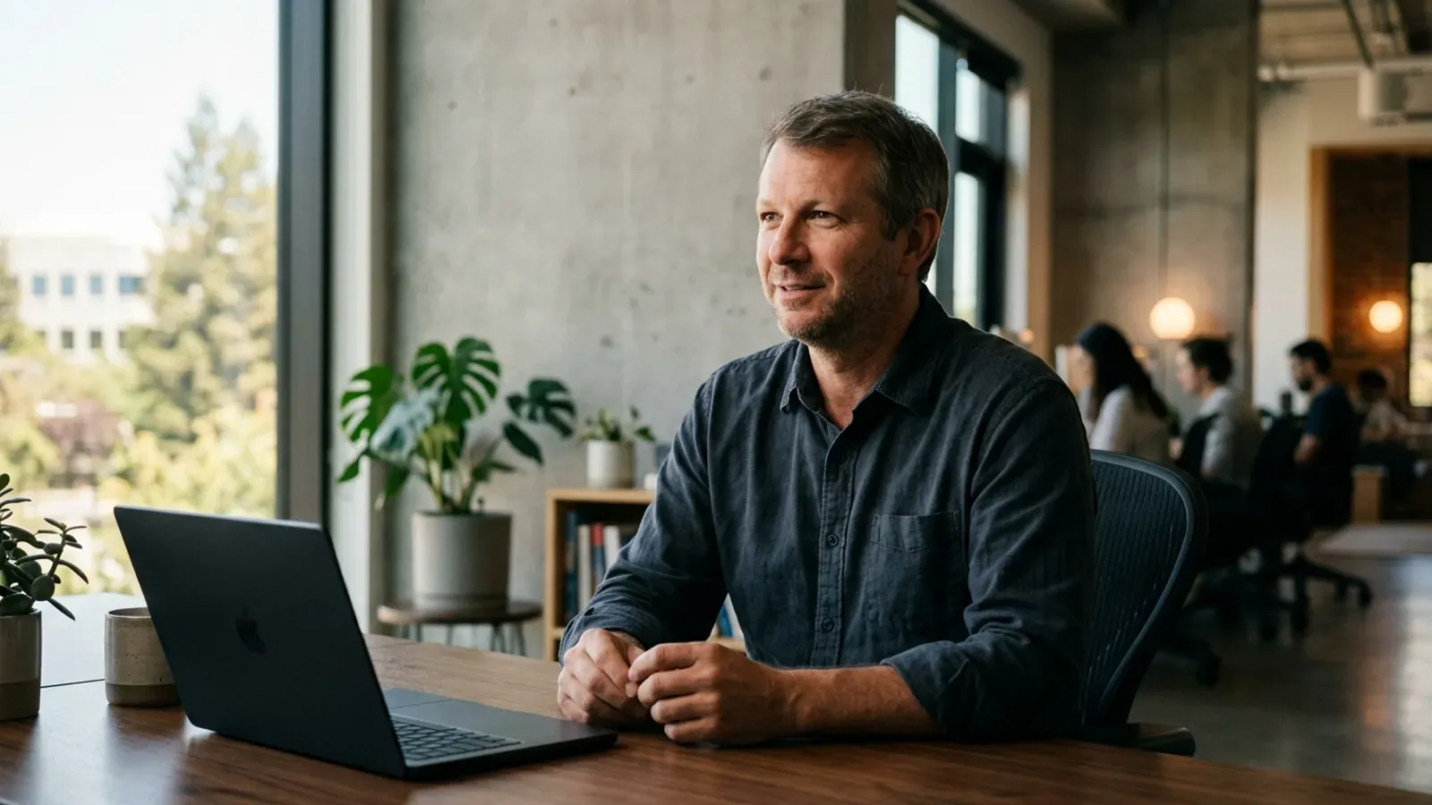 Brian Acton'ın minimalist bir ofiste açık dizüstü bilgisayarının başında masada oturduğu portresi.