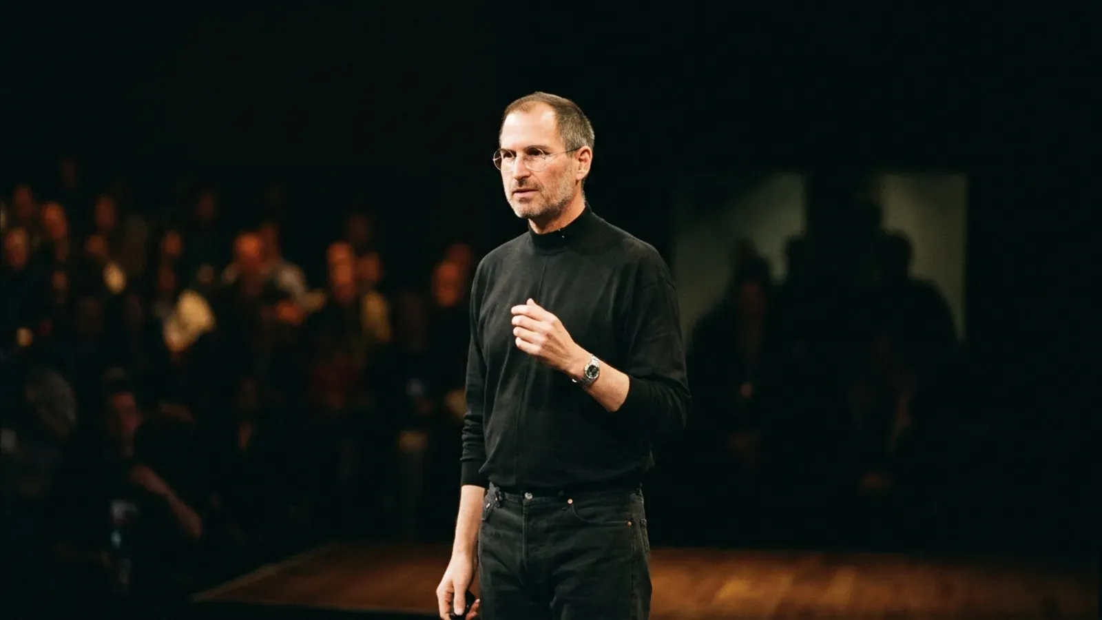 Steve Jobs'un sahnede siyah balıkçı yaka kazağıyla konuşurken çekilmiş portresi.